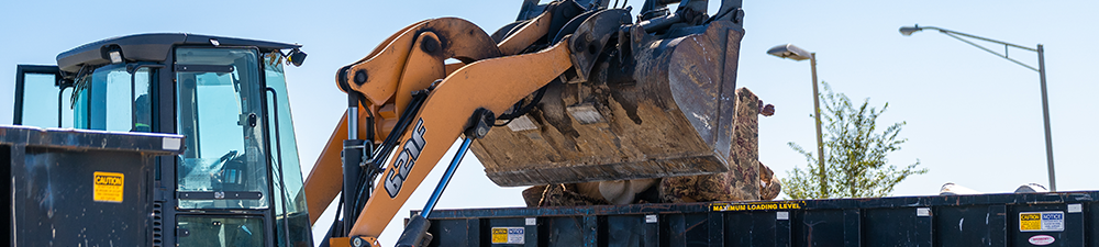 Heavy machinery dumping trash into a dumpster