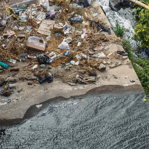 A photograph of trash and litter by a stream of water